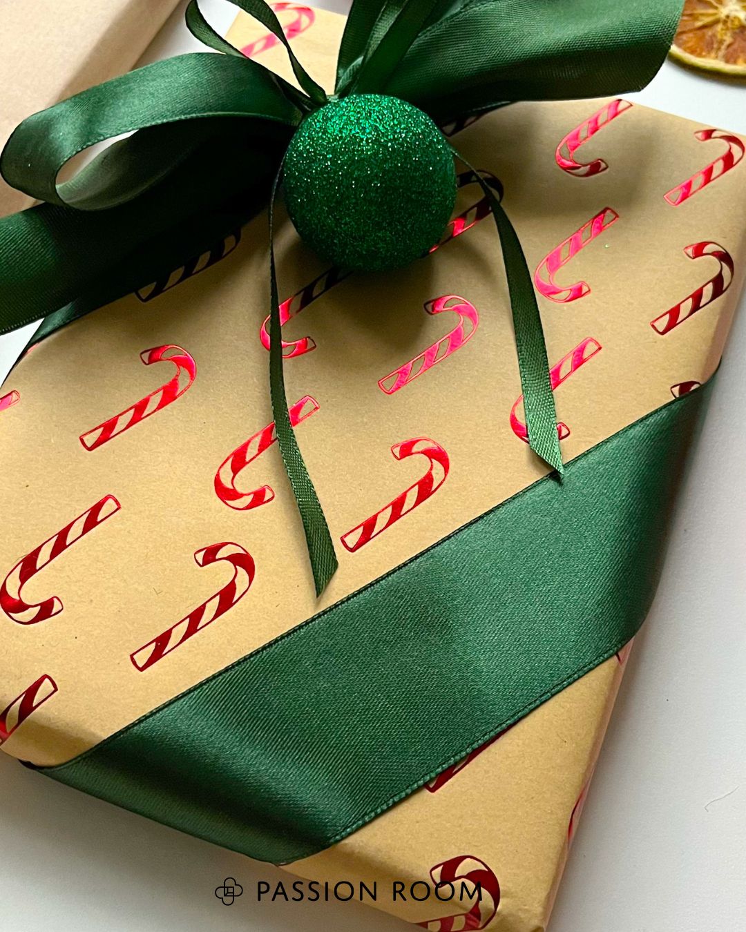 Prezent przepasany zieloną wstążką z kokardą i zawieszką z brokatowej bombki