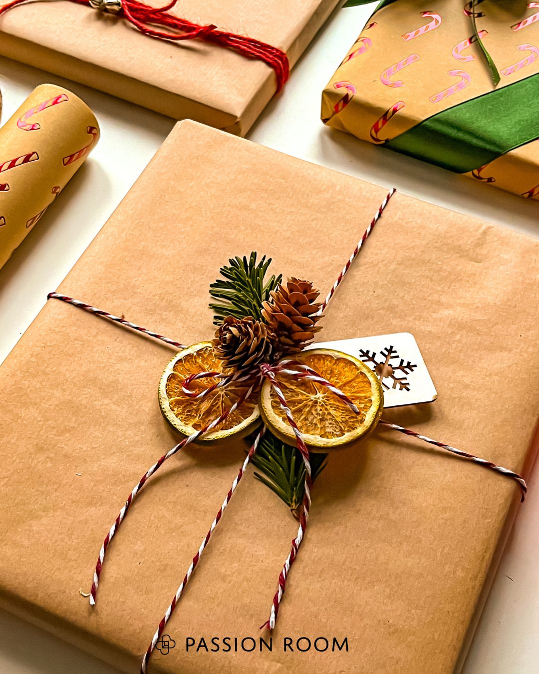 Prezent przewiązany sznurkiem piekarskim w białoczerwonym kolorze przybrany plasterkami suszonej pomarańczy i szyszką 
