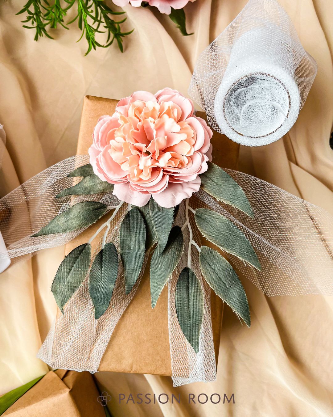 Prezent przewiązany pasmem tiulu przybrany kwiatem i liśćmi tekstylnymi 