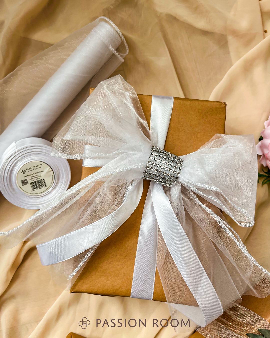 Prezent obwiązany biała wstążką przybrany kokardą z organzy i taśmy diamentowej